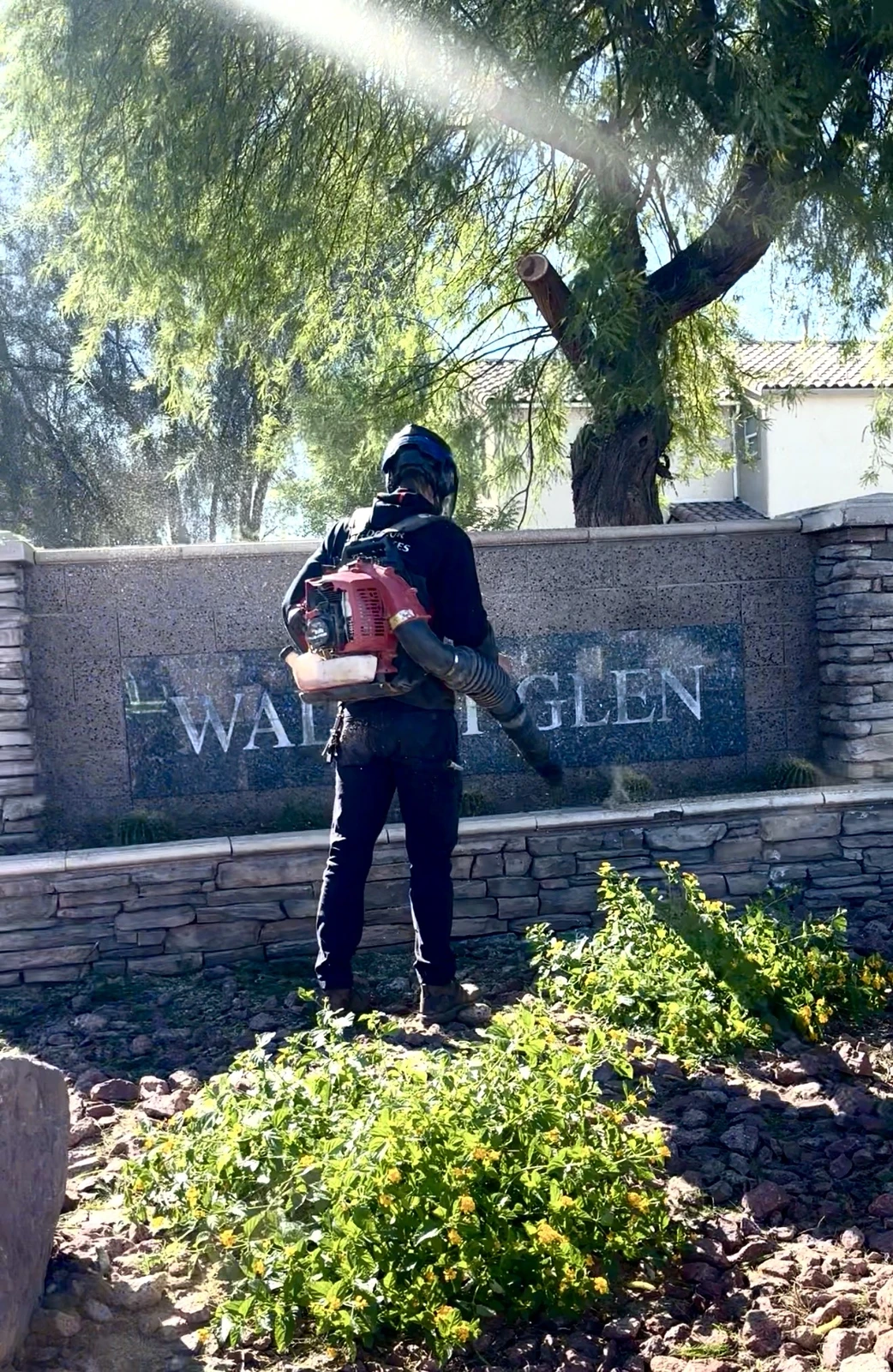 Crew member trimming shrubs at a community entrance monument sign