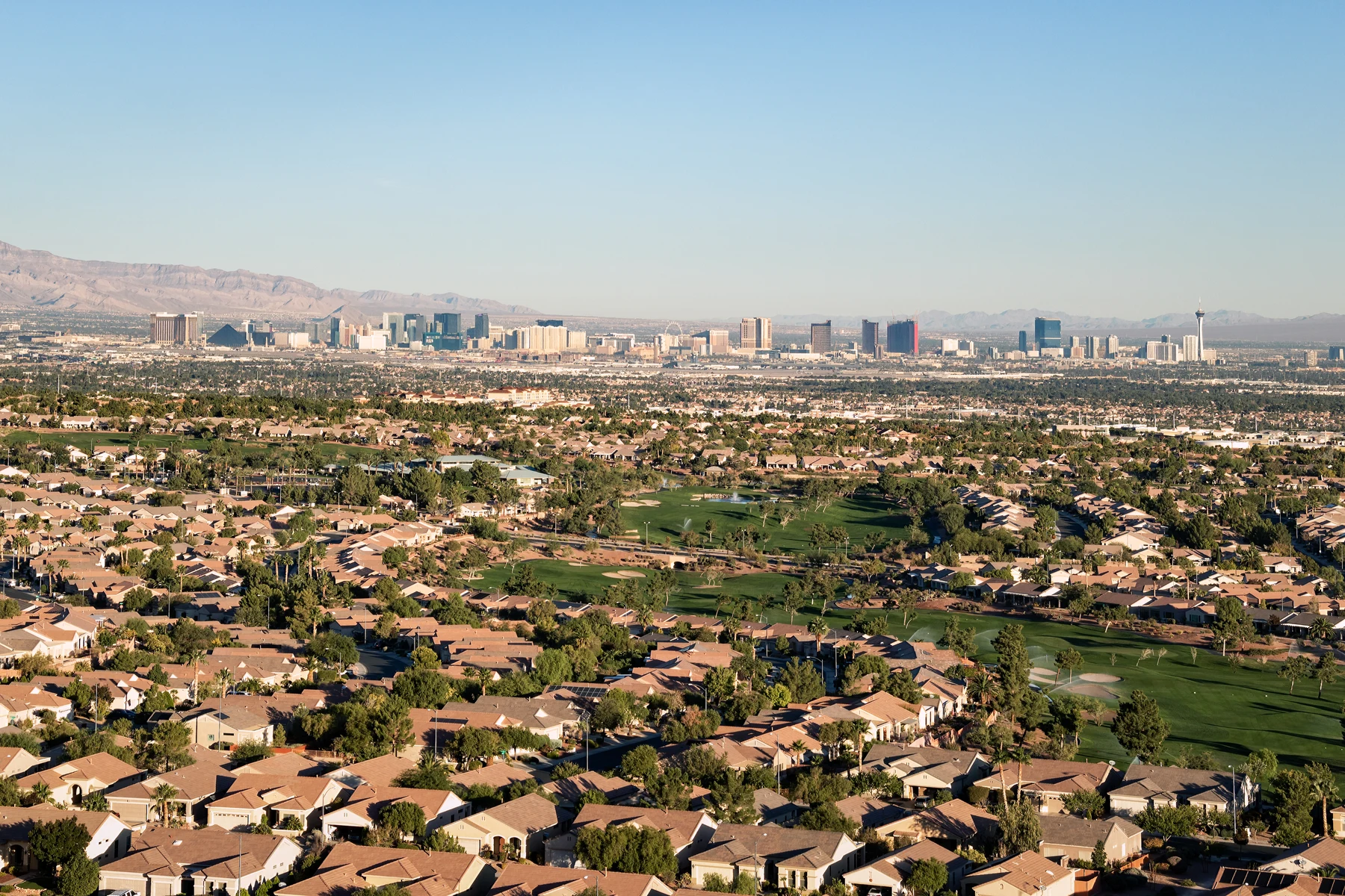 Aerial view of a Las Vegas Valley suburb and golf course with the Strip skyline in the distance