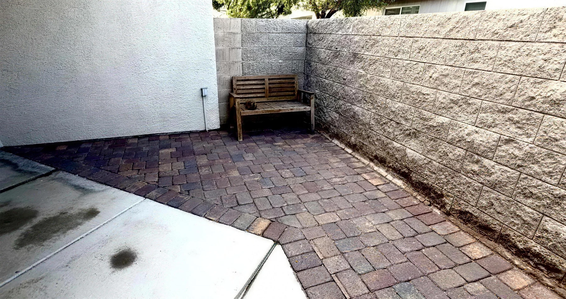The same front yard corner after paver installation, same bench and wall