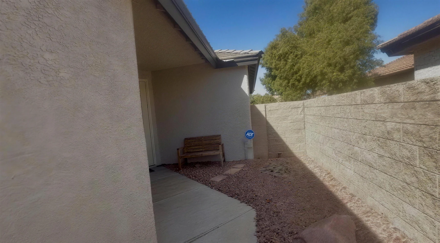 Rock-covered front yard corner with a bench before paver installation