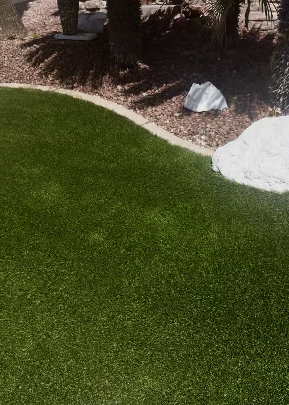 The same edge after artificial turf installation, with matching rock border and boulders
