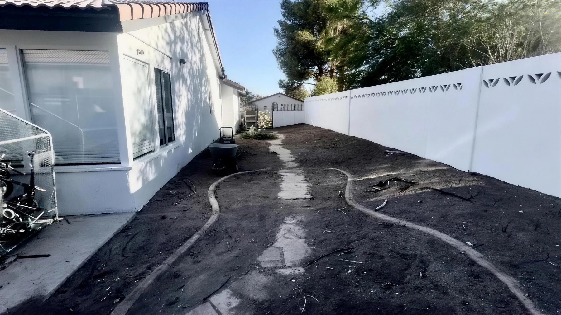 Bare cleared dirt side yard with a curved stepping-stone path before xeriscape installation